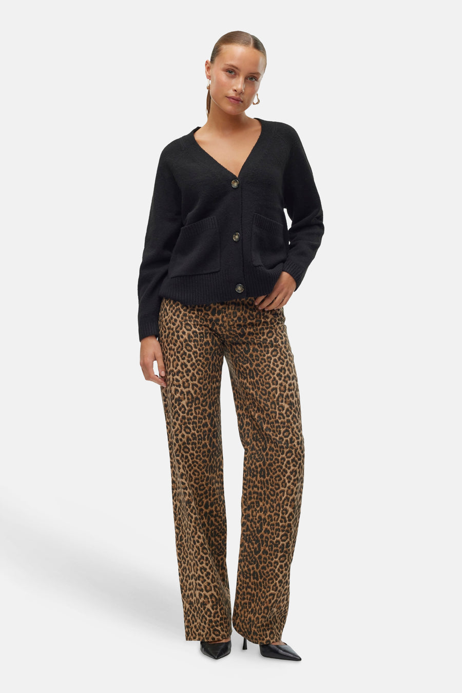 Zwarte cardigan van Vero Moda, met opgestikte zakken en bruine knopen, gedragen over een luipaardbroek.