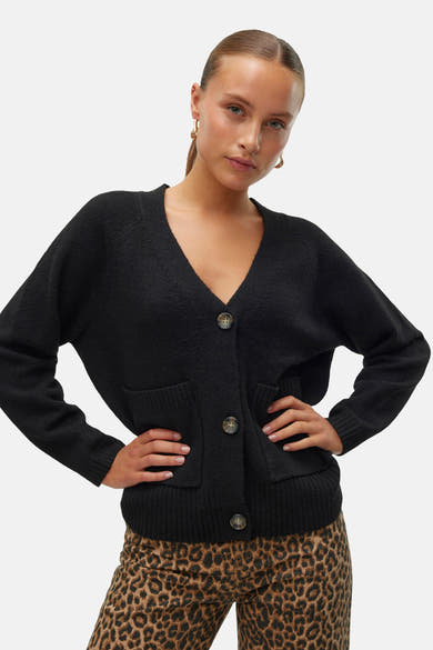 Zwarte cardigan van VERO MODA, met knopen en zakken, gedragen over een broek met luipaardprint.