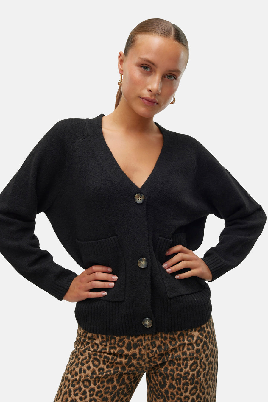 Zwarte cardigan van VERO MODA, met knopen en zakken, gedragen over een broek met luipaardprint.