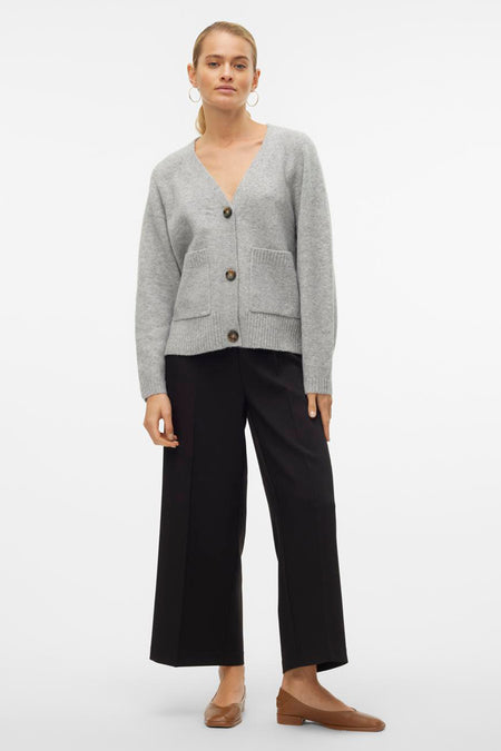 Cardigan gris par VERO MODA, avec boutons marron, poches plaquées, porté avec un pantalon noir et des chaussures marron.