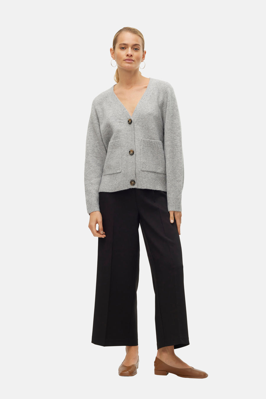 Cardigan gris de VERO MODA avec des poches plaquées et porté avec un pantalon noir et des chaussures marron.
