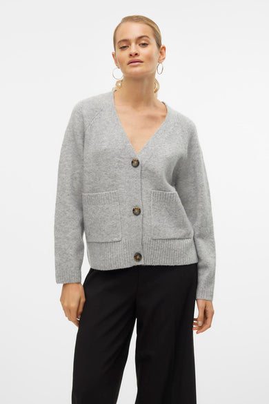 Grijze gebreide cardigan van VERO MODA, met bruine knopen en opgestikte zakken, gedragen met een zwarte broek.