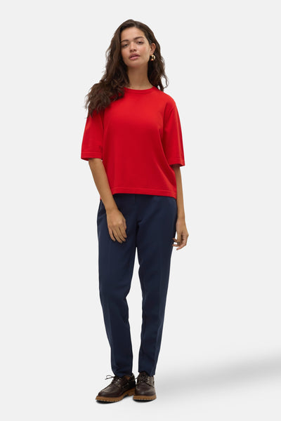 Pull à col rond rouge de VERO MODA® porté avec un pantalon bleu marine et des chaussures en cuir marron.