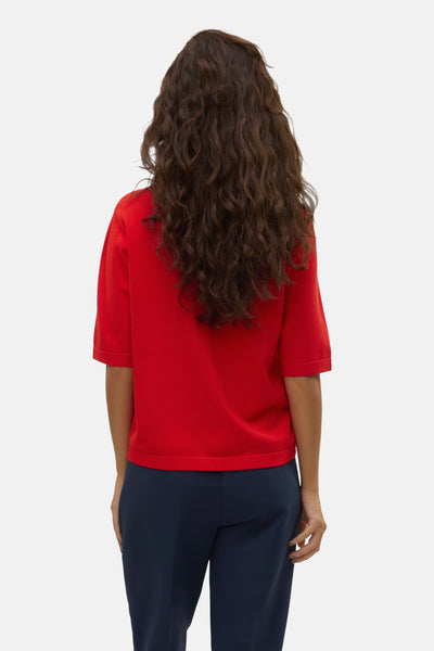 Pull rouge à col rond de VERO MODA, porté avec un pantalon bleu marine, vue de dos, cheveux bruns et bouclés.
