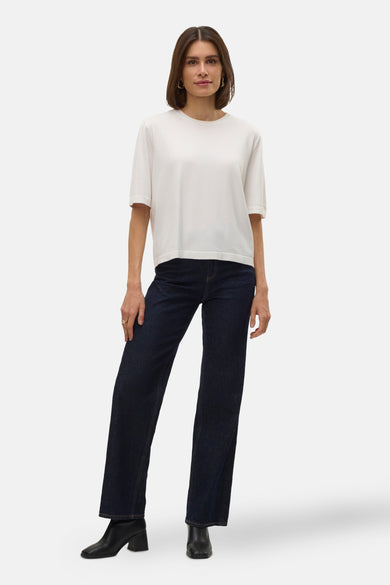 Pull à col rond blanc de VERO MODA, porté avec un jean bleu marine et des bottines noires à talons carrés.