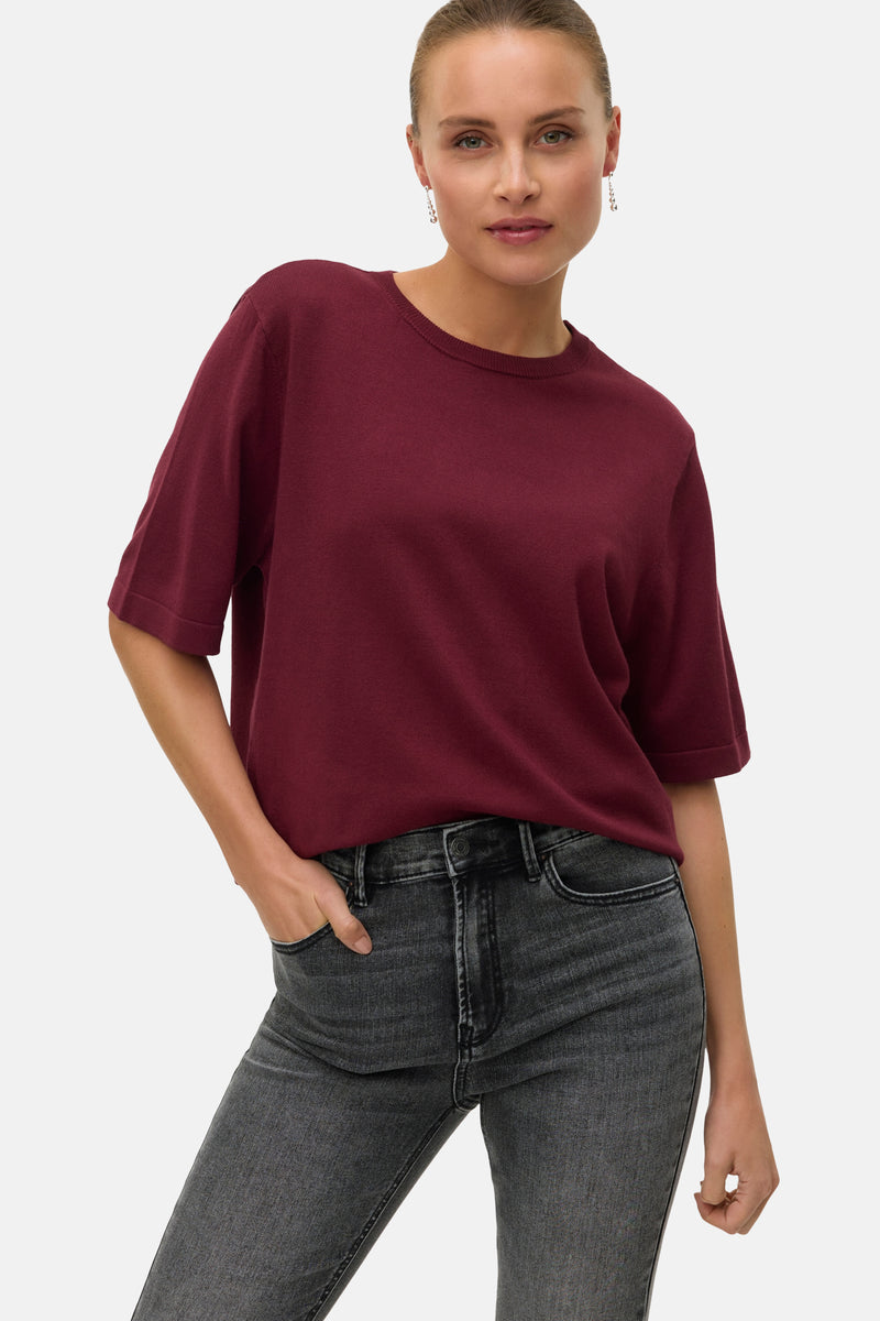 Pull bordeaux à col rond de VERO MODA, porté avec un jean gris délavé, main dans la poche.