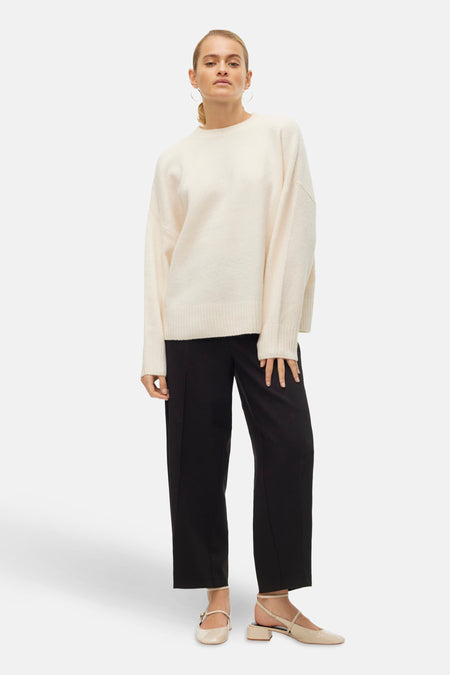 Ecru ronde hals trui van VERO MODA, gedragen met een zwarte broek en crèmekleurige sandalen met bandjes.