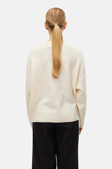 Pull à col rond écru de VERO MODA, porté avec un pantalon noir ample et des boucles d'oreilles créoles, vue de dos.
