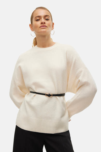Pull à col rond écru de Vero Moda, porté avec une ceinture noire fine, et des boucles d'oreilles créoles dorées.