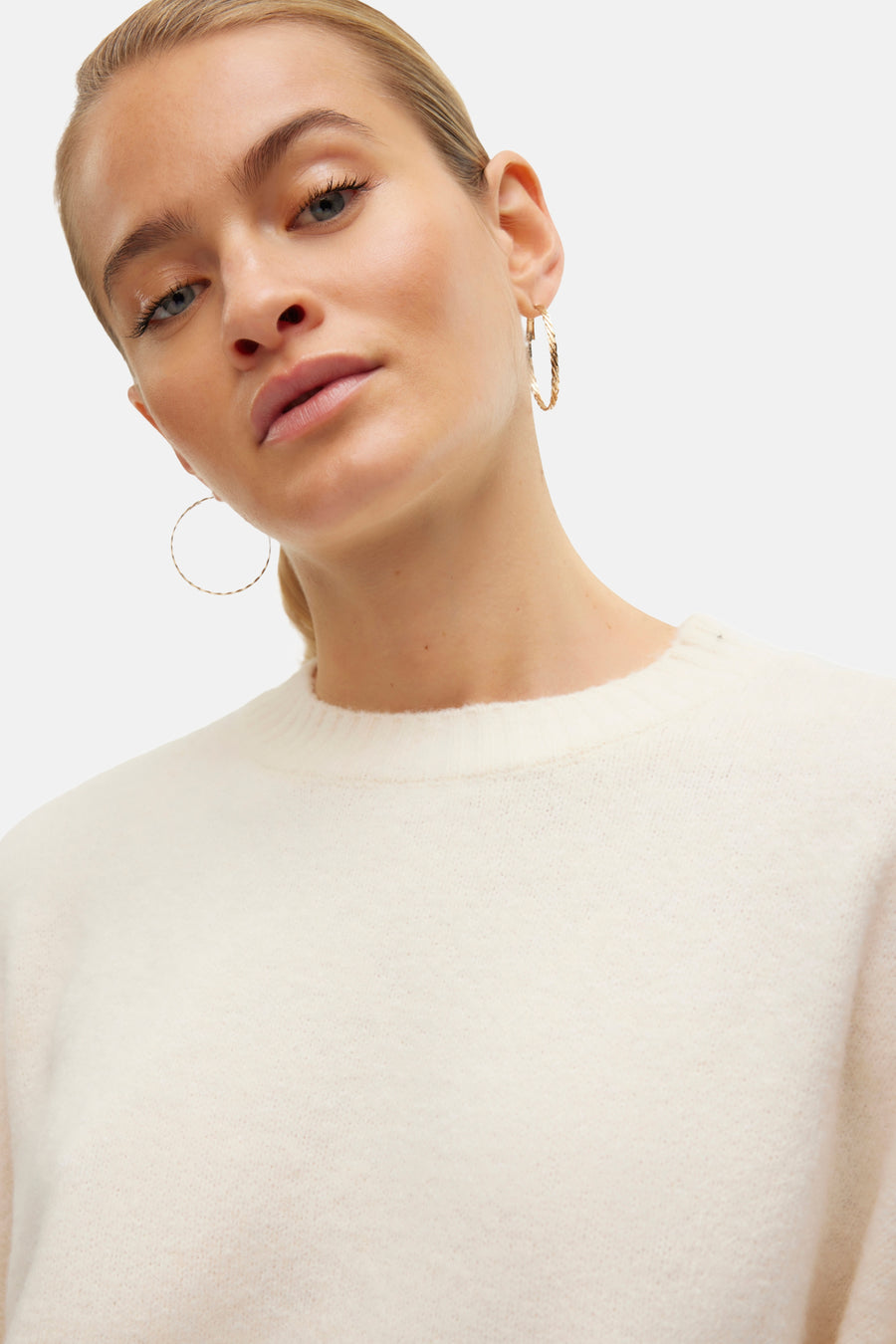 Pull à col rond écru de VERO MODA, texture douce, porté avec des boucles d'oreilles dorées.