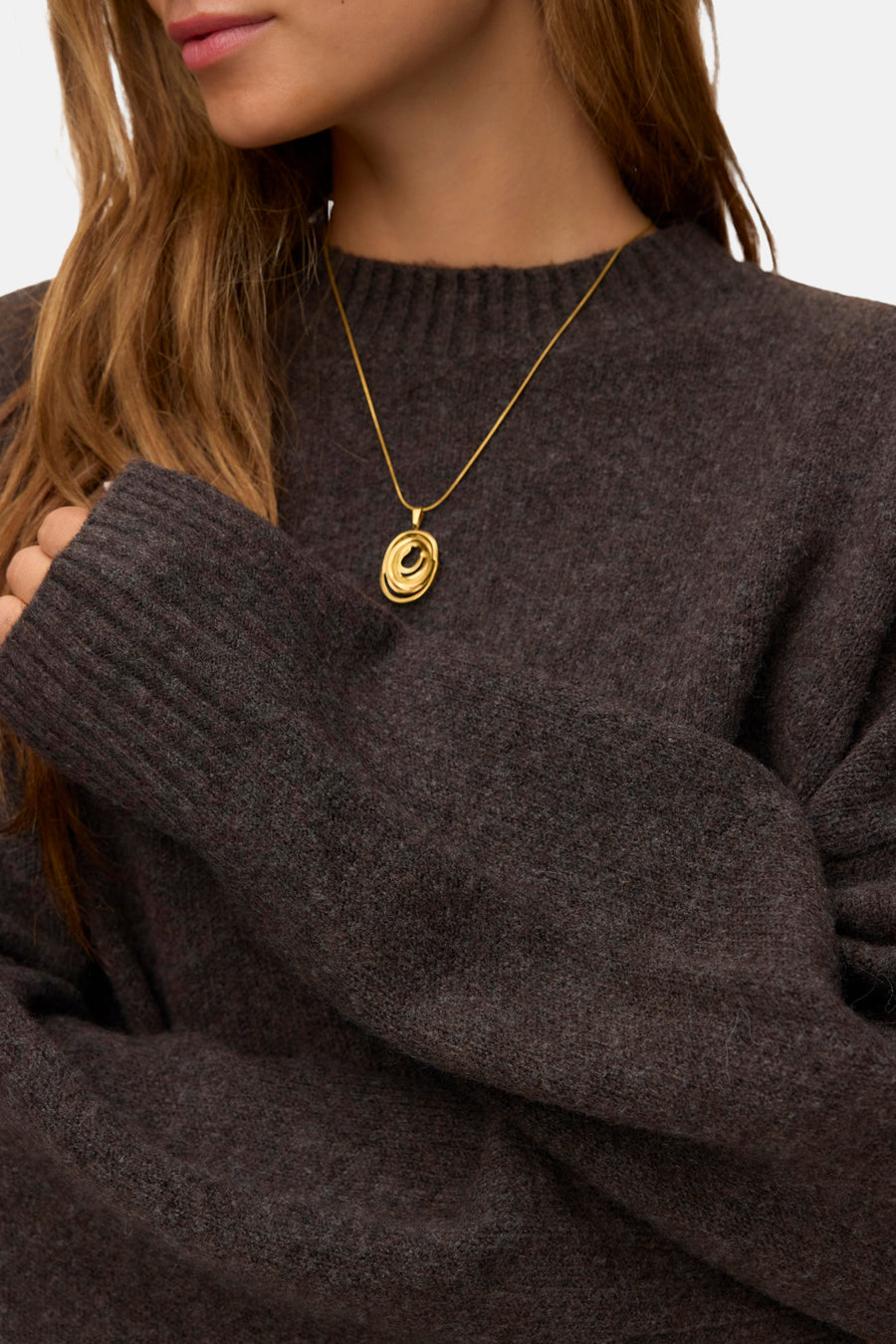 Chocolate torte round-neck sweater with ribbed cuffs and neckline, soft marled texture, worn with gold spiral pendant necklace, close-up front view
