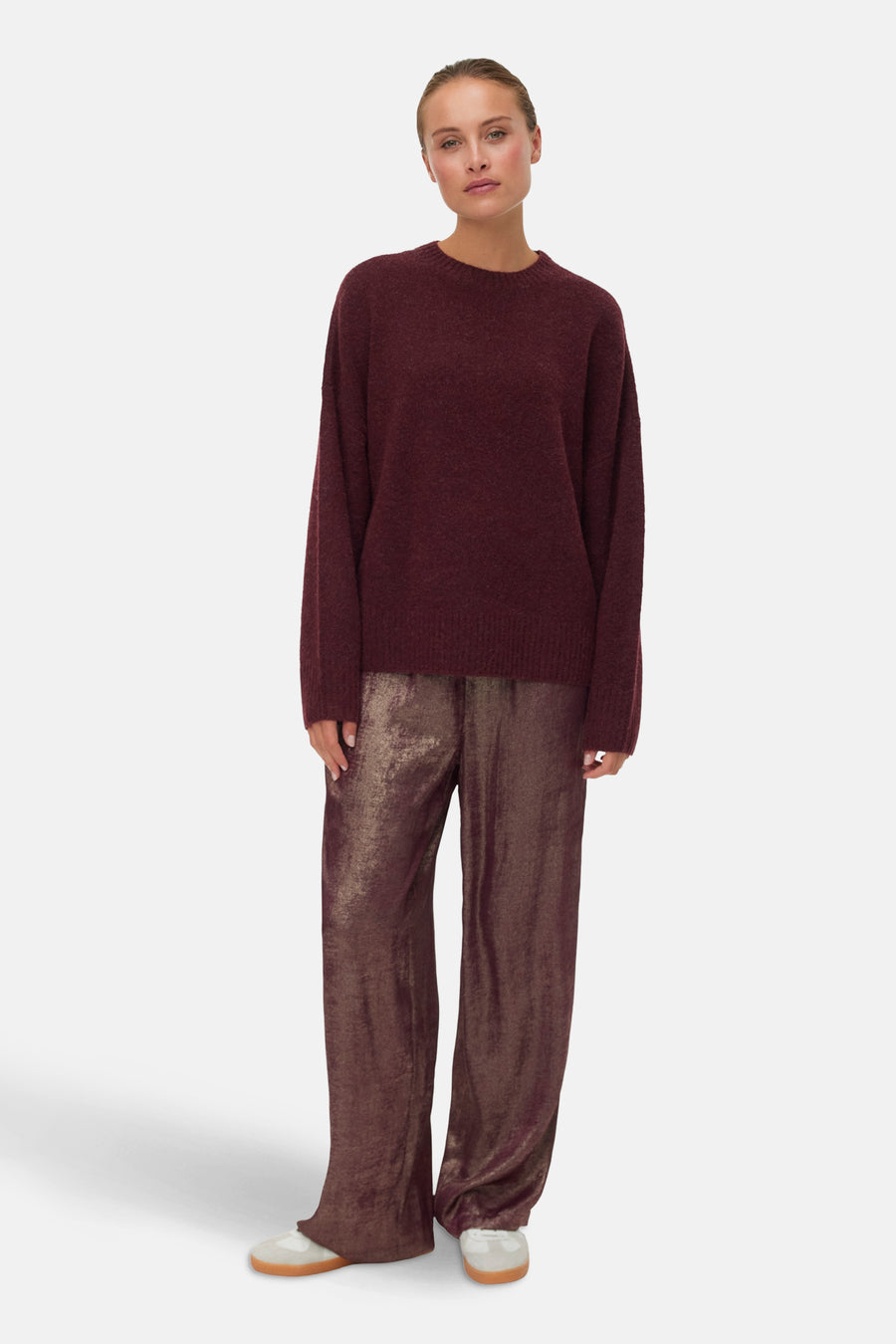 Pull à col rond bordeaux de Vero Moda, porté avec un pantalon brillant couleur bronze.