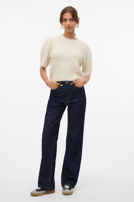 Pull à col rond écru de VERO MODA®, porté avec un jean bleu foncé et des chaussures de sport.
