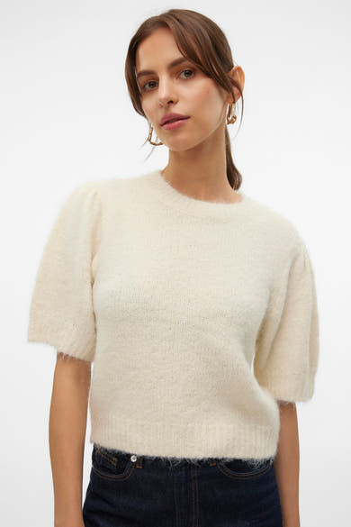 Pull à col rond écru de VERO MODA® porté avec un jean bleu foncé et des boucles d'oreilles dorées.
