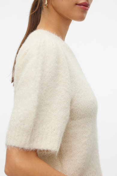 Pull à col rond écru de VERO MODA, manches courtes bouffantes, en maille duveteuse, porté avec des boucles d'oreilles dorées.
