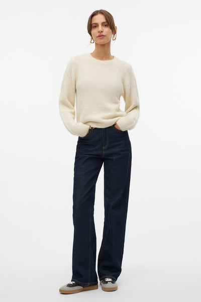 Pull écru à col rond de VERO MODA, porté avec un jean bleu foncé et des baskets neutres.
