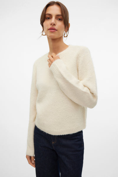 Pull à col rond écru de Vero Moda, porté avec un jean bleu foncé et des boucles d'oreilles dorées.