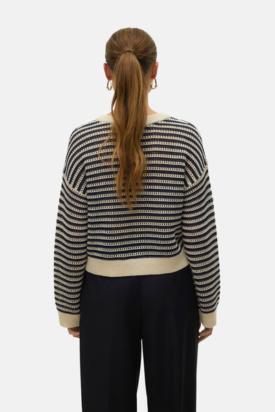 Pull à col rond écru de VERO MODA, rayures horizontales bleu marine, coupe courte et pantalon noir.

