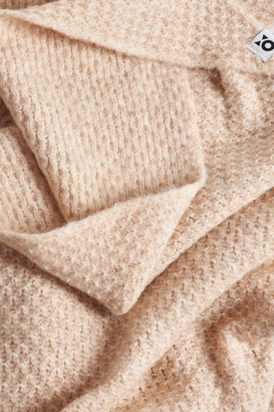 Écharpe beige en maille torsadée de OPUS, texture douce et moelleuse, pliée en plusieurs couches.
