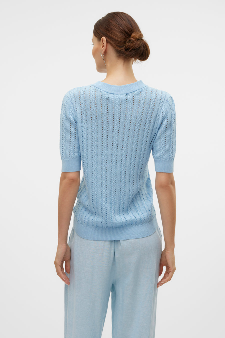 Pull bleu à col rond de VERO MODA, avec des détails ajourés et manches courtes, porté avec un pantalon bleu.
