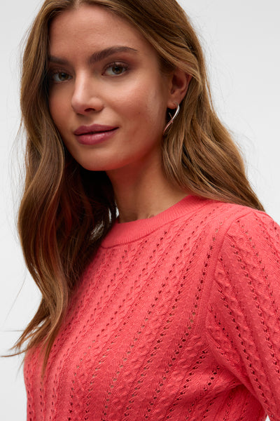 Pull corail à col rond de VERO MODA, avec motifs ajourés, porté avec des boucles d'oreilles argentées.
