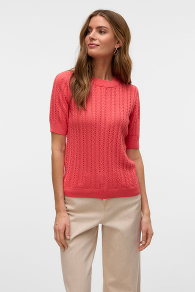 Koraalkleurige trui met ronde hals van VERO MODA, met ajourpatroon en gedragen met een beige broek.