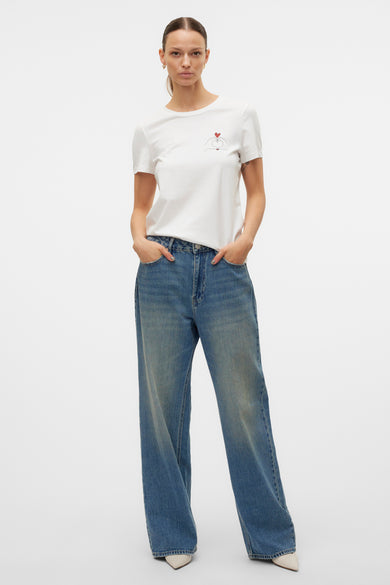 T-shirt à manches courtes blanc par VERO MODA, avec motif cœur stylisé et porté avec un jean ample.
