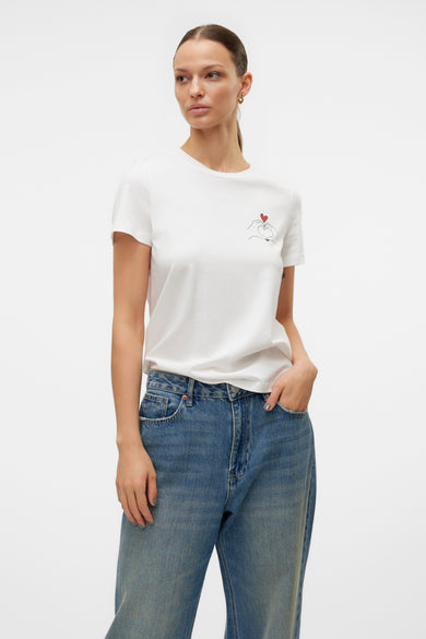 T-shirt blanc à manches courtes de Vero Moda avec motif cœur sur la poitrine, porté avec un jean bleu taille haute.
