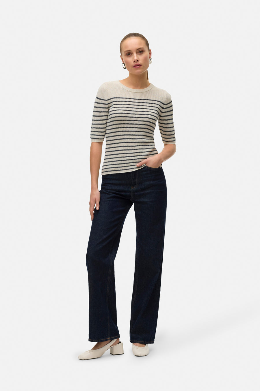 Pull à col rond beige rayé de VERO MODA, porté avec un jean bleu foncé et des escarpins blancs.