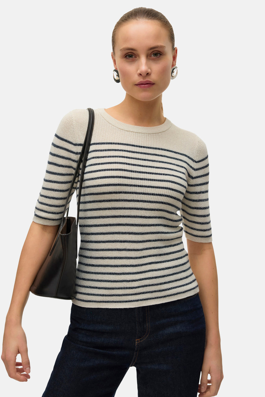 Pull à col rond beige de Vero Moda, à rayures marine, porté avec un jean foncé et des boucles d'oreilles argentées.