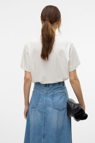 T-shirt blanc à manches courtes de VERO MODA, porté avec une jupe longue en jean bleu et un sac noir.
