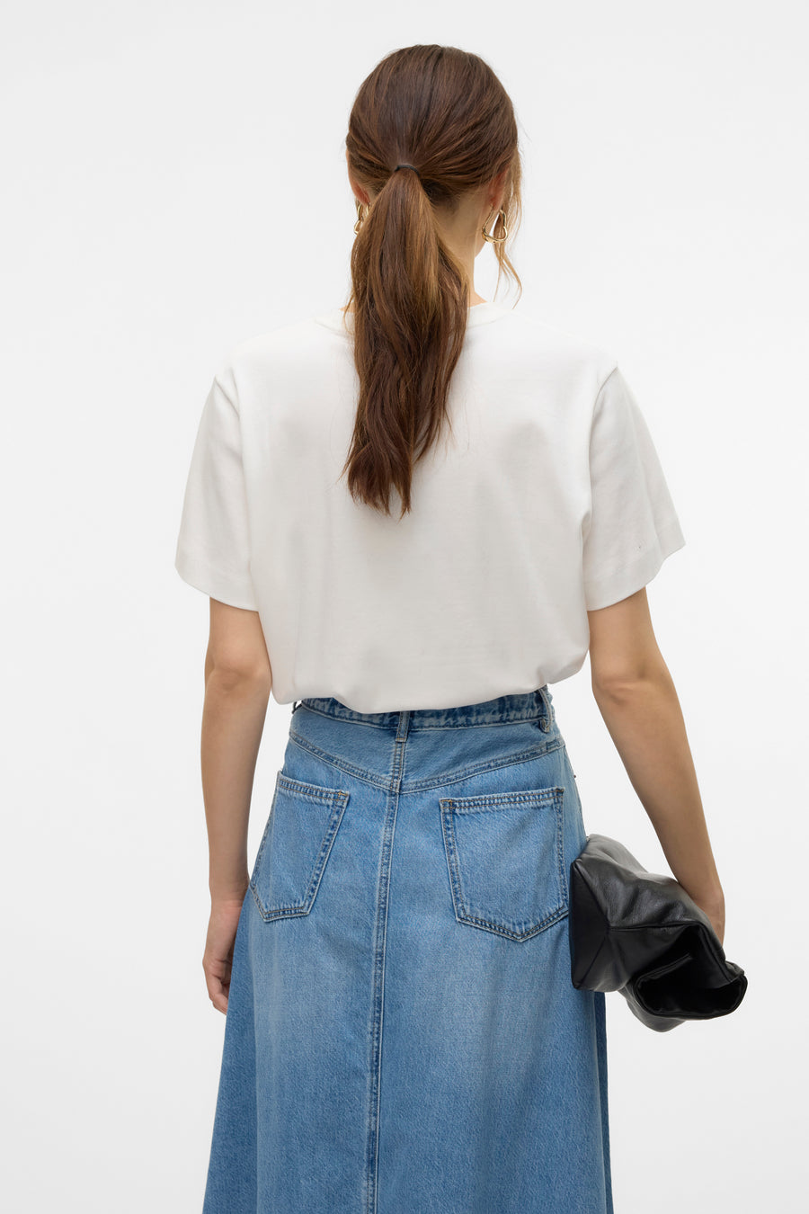 T-shirt blanc à manches courtes de VERO MODA, porté avec une jupe longue en jean bleu et un sac noir.
