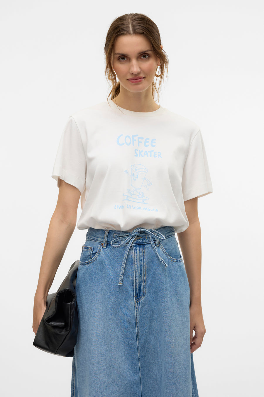 T-shirt à manches courtes blanc de VERO MODA® avec imprimé « Coffee Skater » porté avec une jupe en jean.

