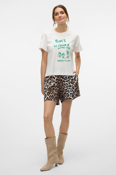 T-shirt blanc à manches courtes de VERO MODA, avec un imprimé décoratif sur le devant, porté avec un short à motif léopard.