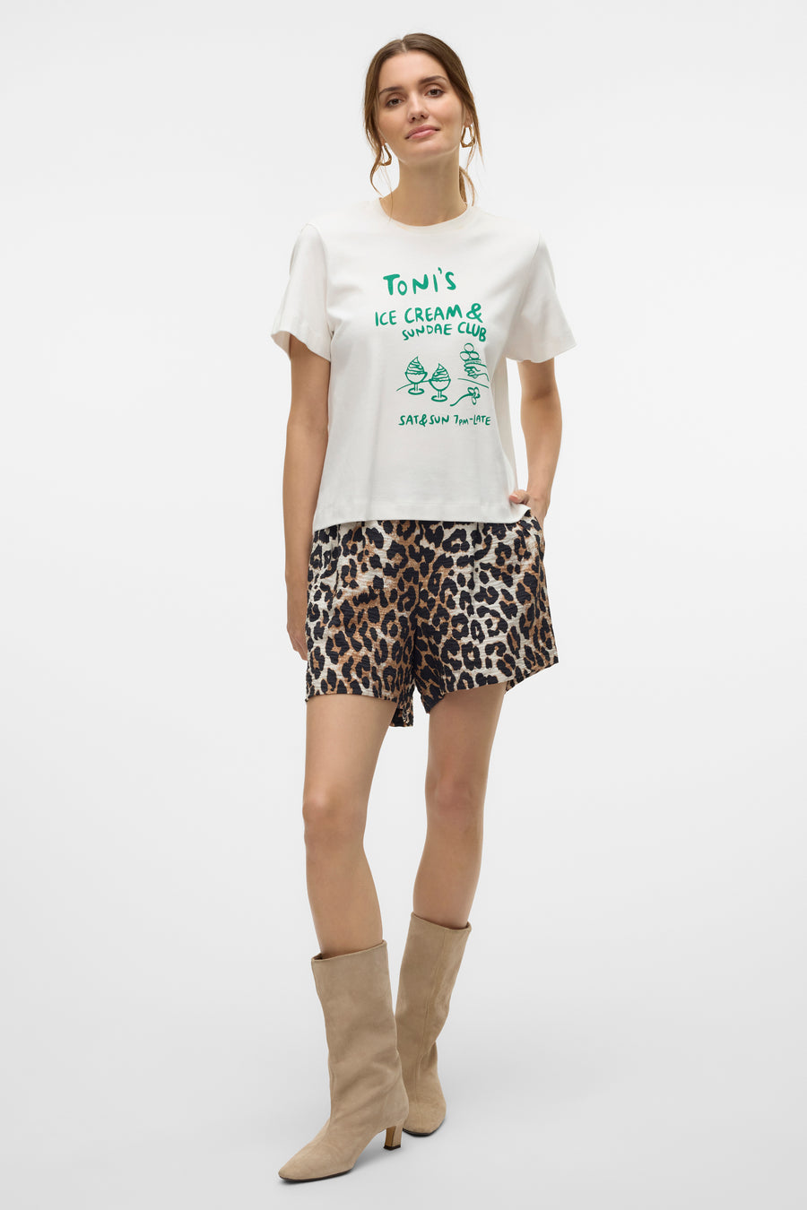 T-shirt blanc à manches courtes de VERO MODA, avec un imprimé décoratif sur le devant, porté avec un short à motif léopard.