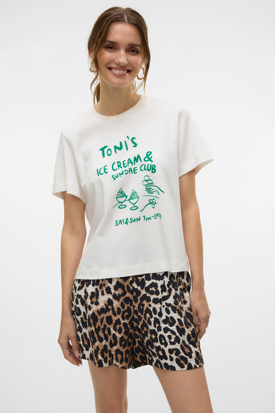 T-shirt blanc à manches courtes de VERO MODA, imprimé avec un motif de club de crème glacée, porté avec un short à imprimé léopard.
