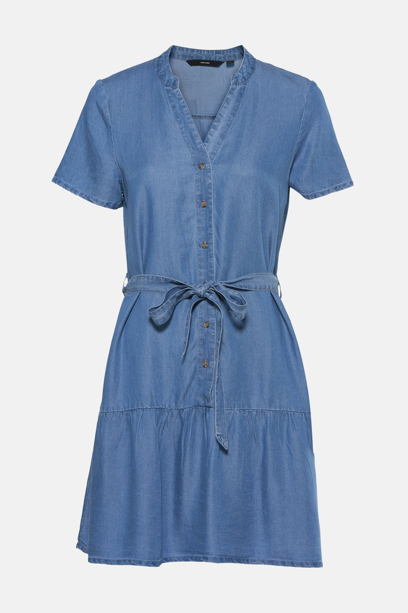 Robe courte en jean bleu moyen de VERO MODA® avec col en V, patte de boutonnage, manches courtes, ceinture à nouer et jupe à volants.