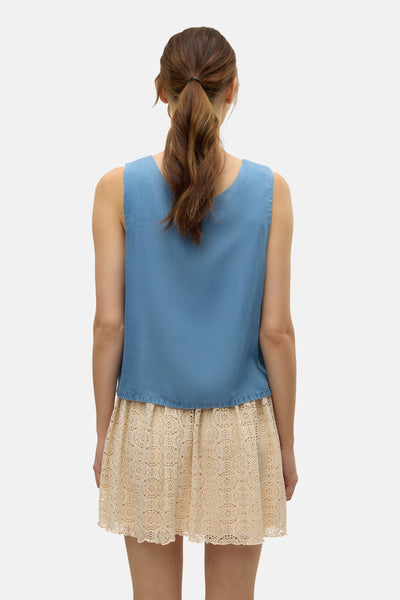Blouse bleue sans manches de VERO MODA, portée avec une jupe beige à dentelle.