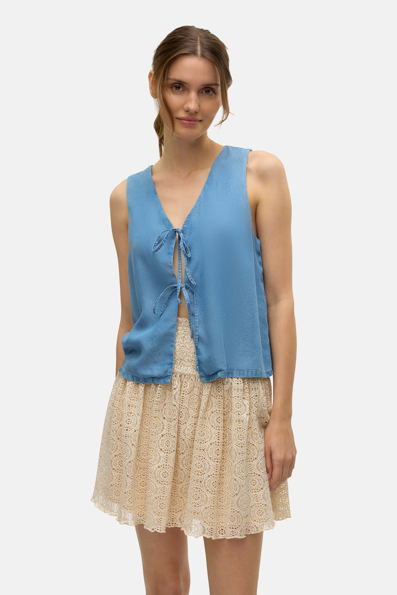 Blouse bleue à nouer de VERO MODA, portée avec une jupe courte en dentelle beige.
