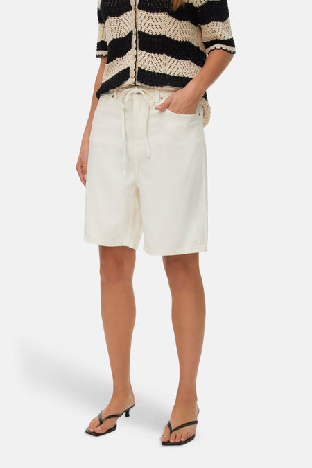 Short écru de VERO MODA, porté avec un haut rayé et des chaussures à talons.
