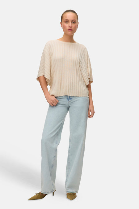 Pull beige côtelé de VERO MODA, porté avec un jean bleu clair et des escarpins à nœud vert olive.

