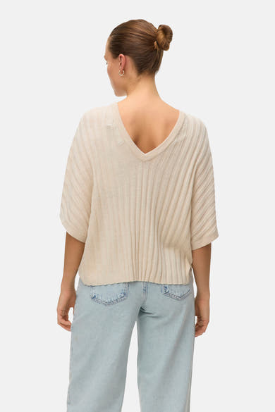 Pull beige à col en V de VERO MODA®, en tricot côtelé, porté avec un jean bleu clair taille haute, vue de dos.

