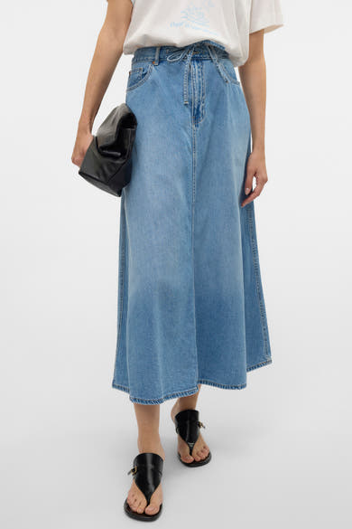 Middelblauwe lange spijkerrok van Vero Moda, gedragen met een wit T-shirt en zwarte sandalen.