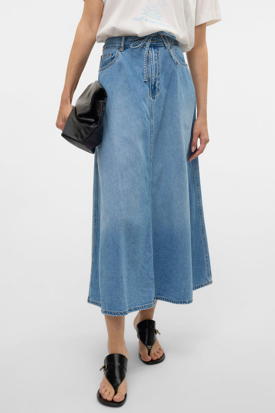 Middelblauwe lange spijkerrok van Vero Moda, gedragen met een wit T-shirt en zwarte sandalen.