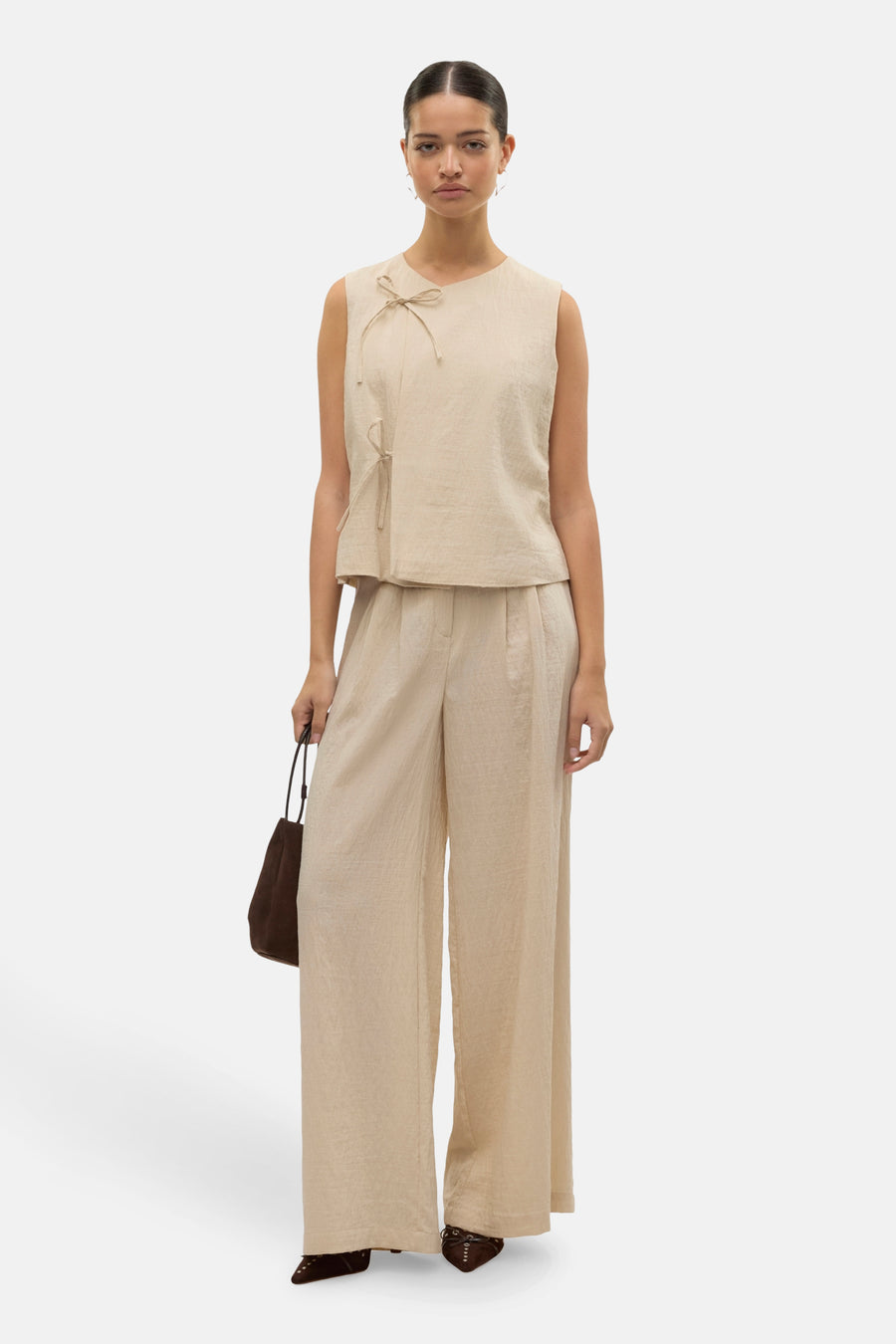 Pantalon beige de VERO MODA, avec une coupe ample et porté avec un haut assorti et un sac à main.
