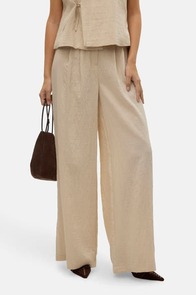 Pantalon beige de VERO MODA, ample et fluide, porté avec un haut assorti et un sac marron.
