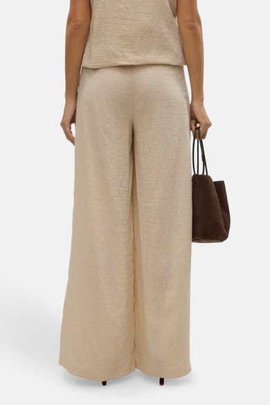 Pantalon large beige de VERO MODA, avec un sac marron porté à la main, vue de dos.
