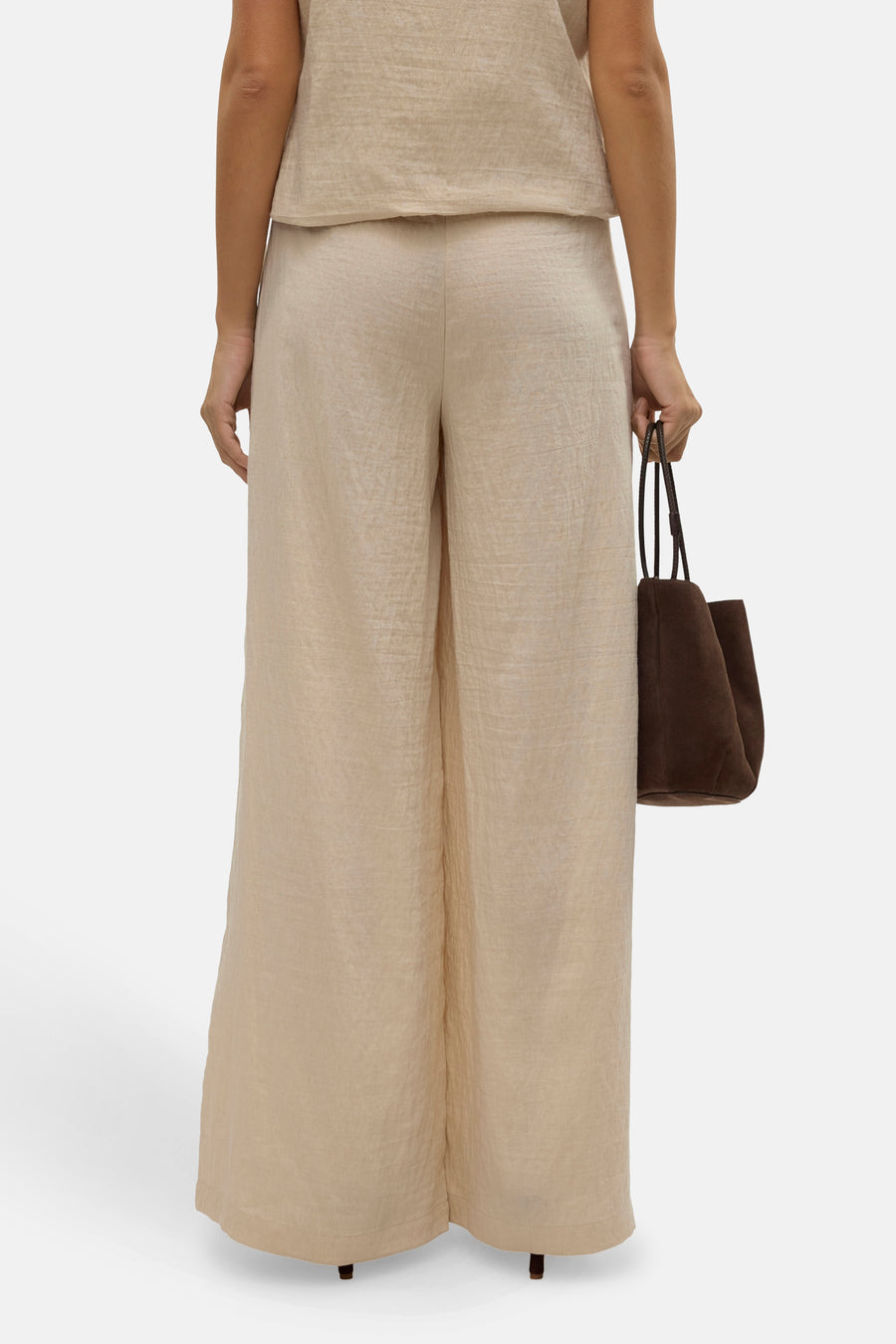 Pantalon large beige de VERO MODA, avec un sac marron porté à la main, vue de dos.
