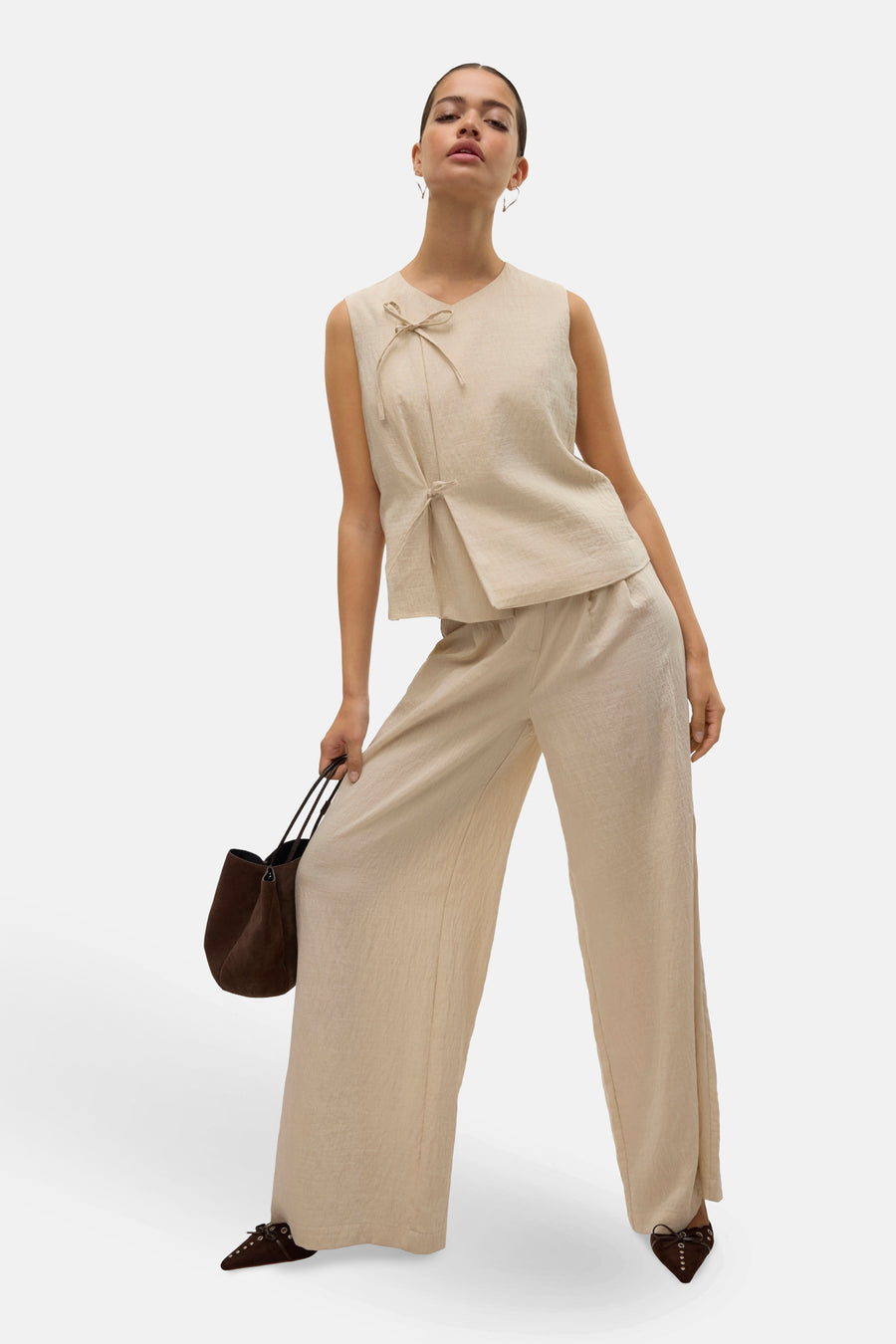 Pantalon beige de VERO MODA, ample, avec un haut beige noué, un sac à main marron et des chaussures originales.
