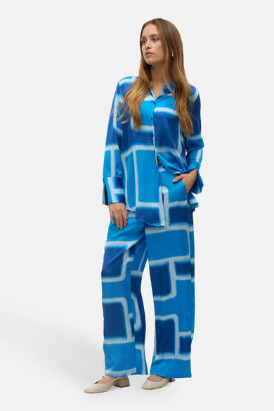 Blauwe broek van VERO MODA, met geometrische patronen, losse en vloeiende pasvorm, gedragen met neutrale schoenen.